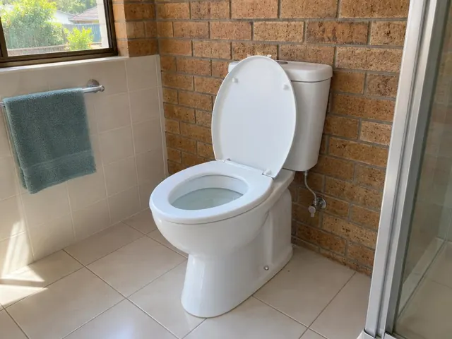 Clean white toilet in a tiled bathroom with brick wall and towel rail in Rouse Hill