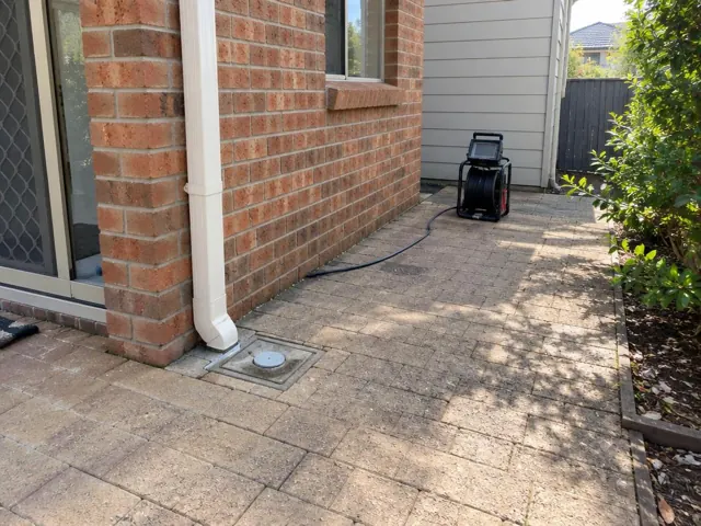Capped drain inspection opening beside a brick wall and paved side path with a camera reel in Rouse Hill